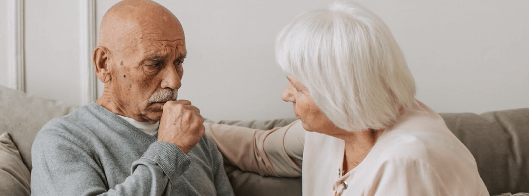 Elderly man coughing whilst being comforted by his wife