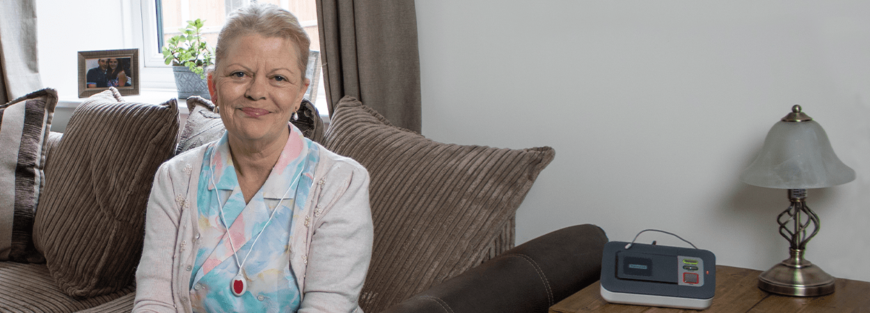 Careline Alarm User sitting on sofa wearing pendant